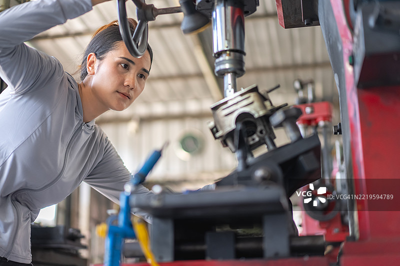 一位自信的年轻女性正在工厂里使用钻床和车床修理摩托车零件。图片素材