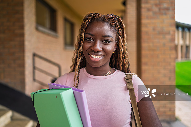 一位快乐的黑人女大学生手拿文件夹，享受着校园时光的肖像图片素材