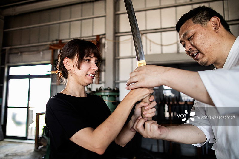 一位旅行者在剑匠工作坊的旅游中试图握住一把日本刀。图片素材