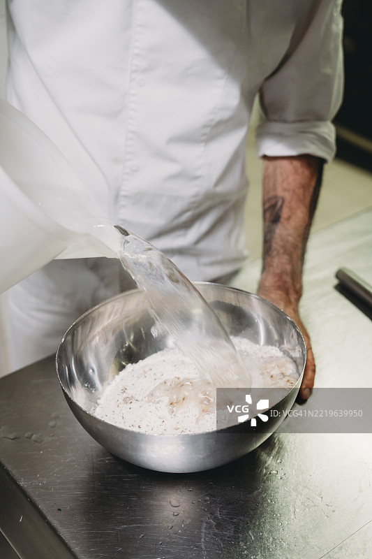 厨师在金属碗中将水倒入面粉中图片素材