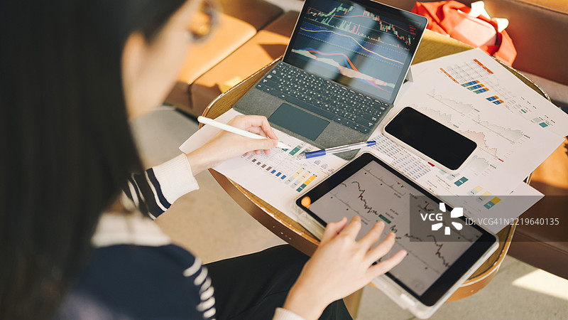 Z世代女性商务专业人士在多任务办公环境中使用智能手机，旁边有笔记本电脑和文件，同时管理工作桌上的图表和报告。图片素材