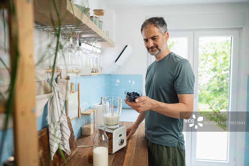 活跃的中年男性在厨房准备健康的蓝莓冰沙，使用新鲜食材图片素材