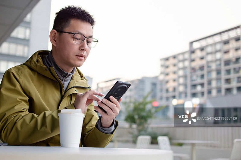 亚洲男子手持咖啡杯使用智能手机图片素材
