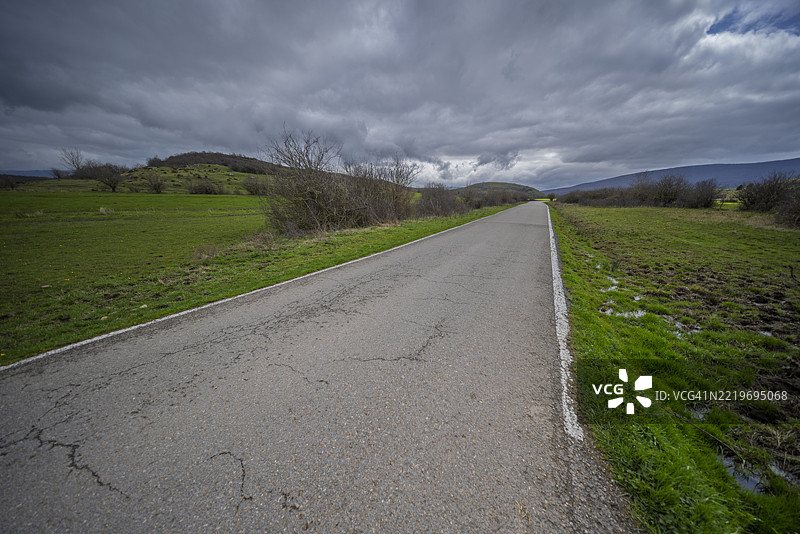 西班牙绿野中的阴云密布的道路图片素材