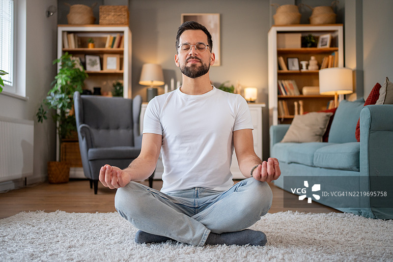 年轻男子在家中的客厅冥想图片素材
