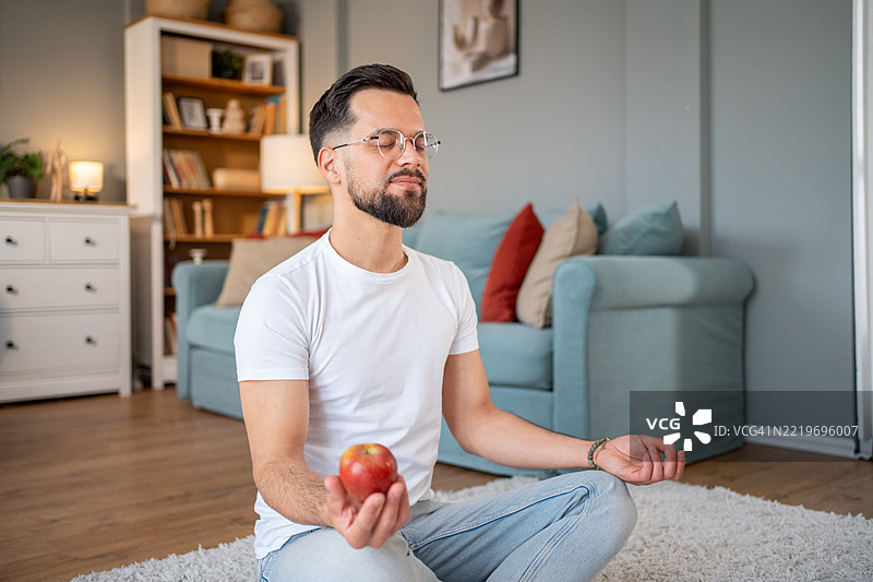 年轻男子在客厅冥想，手中拿着一个苹果图片素材