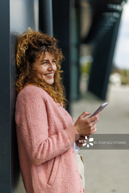 阳光明媚的城市中，微笑的女性在等待朋友时上网冲浪图片素材