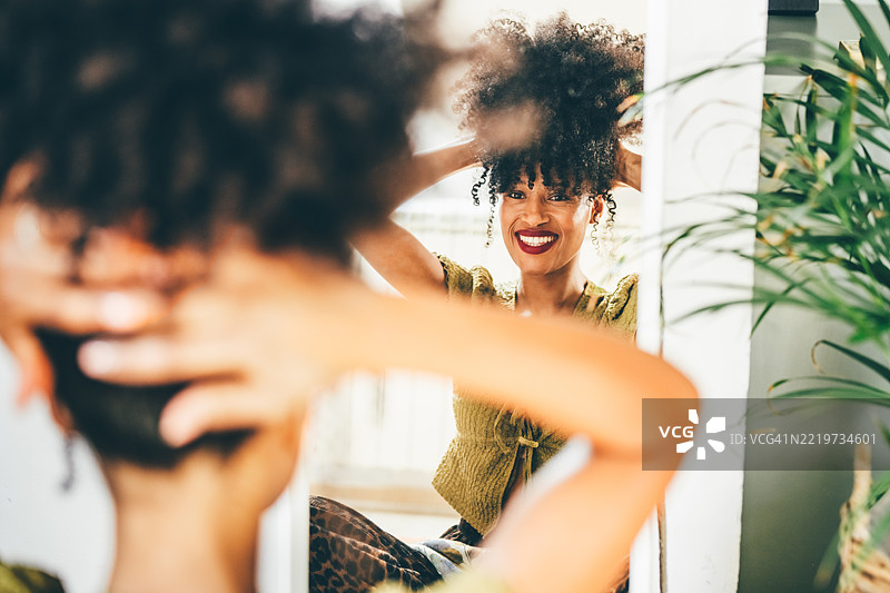 一位女性在镜子前整理她的卷发。图片素材