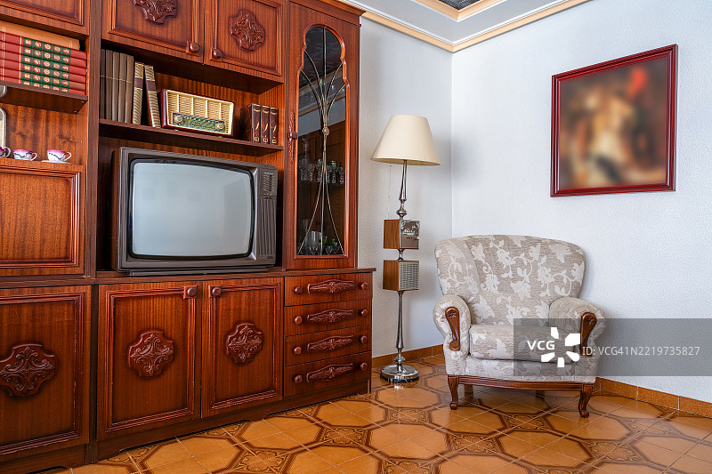 复古风格的客厅，配有复古家具，如木制橱柜、CRT电视、老式收音机、图案扶手椅和落地灯，体现了1980年代的复古风情。图片素材