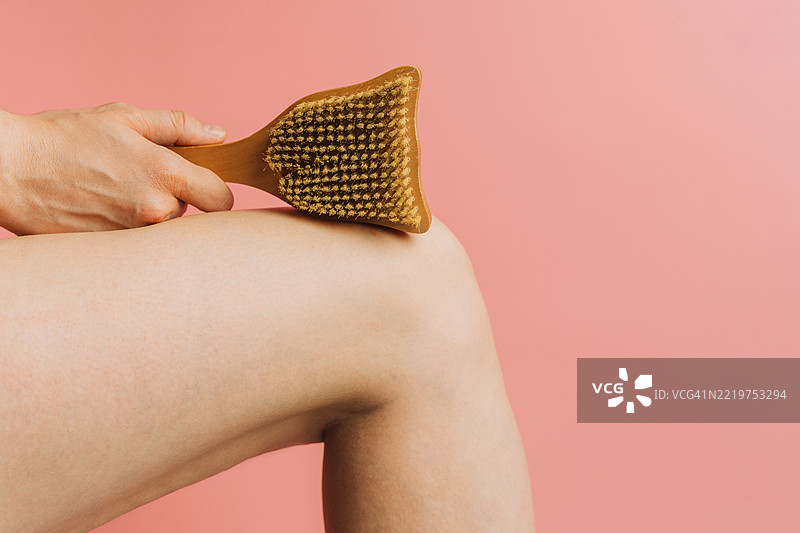 干刷毛刷触碰大腿皮肤的特写，粉色背景图片素材