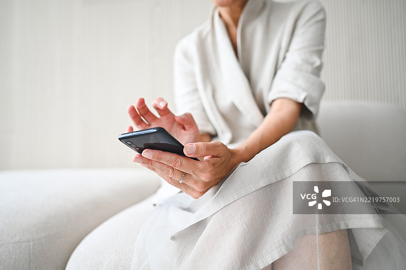 老年女性坐在家中舒适的沙发上，使用手机浏览互联网，享受闲暇时光图片素材