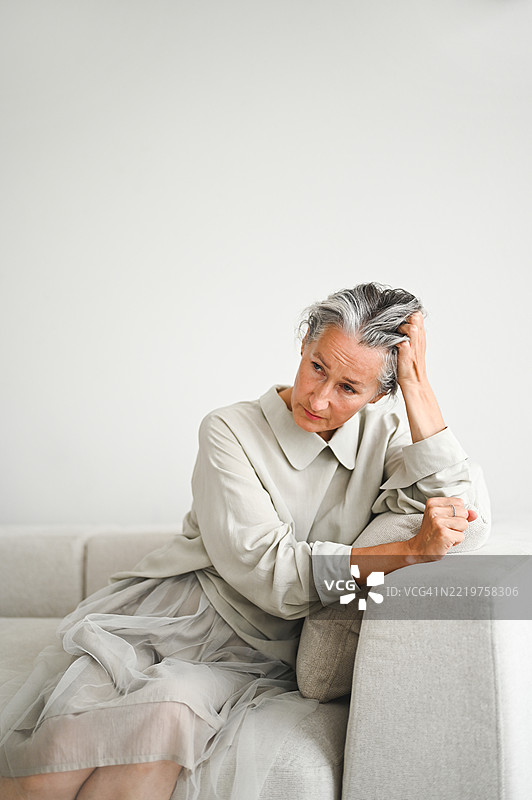 一位老年女性坐在沙发上，手托着头，沉思人生。图片素材