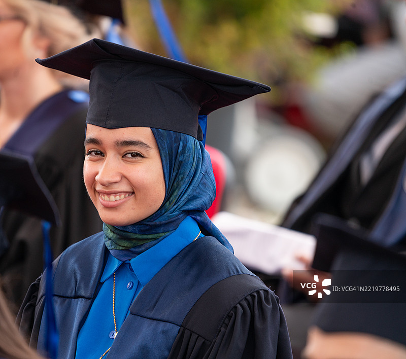 一位微笑的穆斯林女性，穿着毕业袍，在人群中脱颖而出图片素材