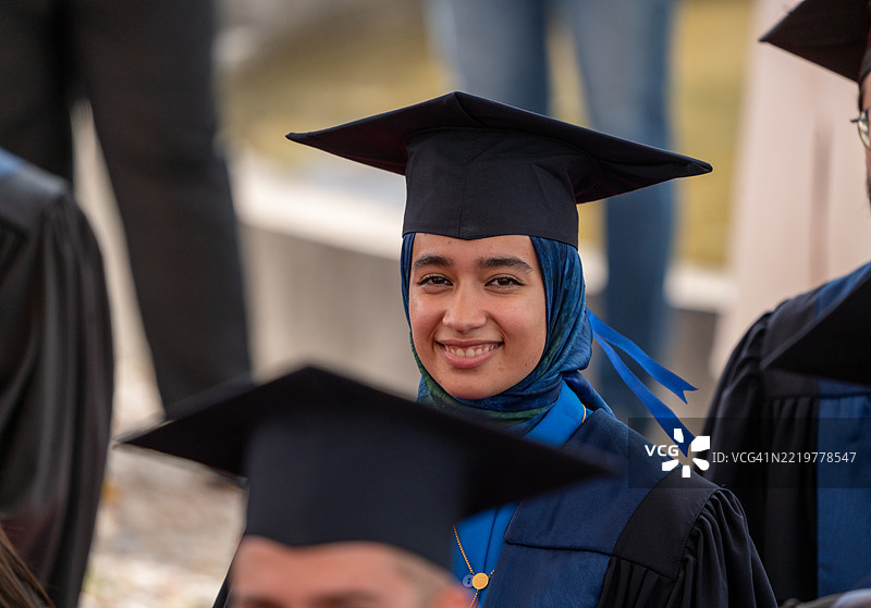 一位微笑的穆斯林女性，穿着毕业袍，在人群中脱颖而出图片素材