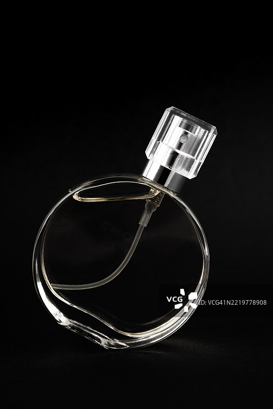 黑色背景上的透明玻璃香水喷雾瓶，瓶内有液体。极简香水静物。图片素材
