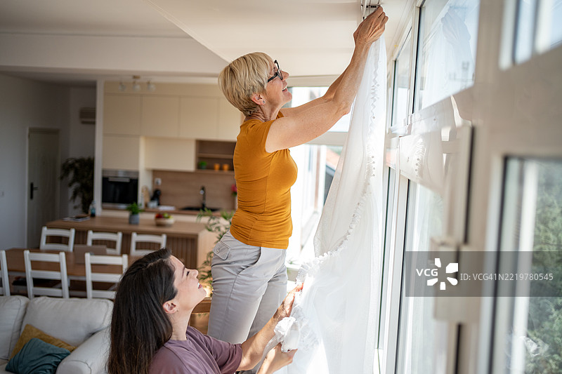 女性在现代公寓中挂窗帘：团队合作与家居装饰图片素材