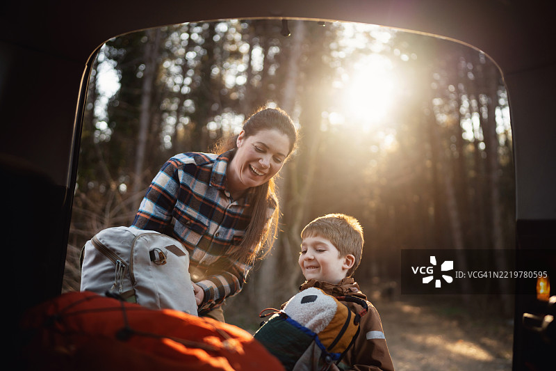 一位妈妈和她的儿子正在从汽车后备厢中取出登山装备，准备开始他们的户外冒险。图片素材
