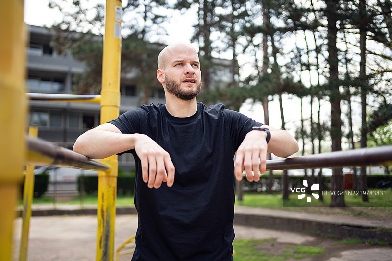 光头男子在城市公园的双杠上进行户外训练图片素材