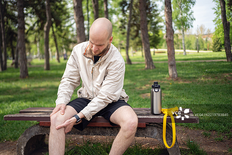 公园长椅上坐着的男人，运动后手里拿着水瓶图片素材