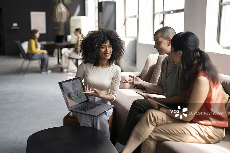 微笑的女商人向办公室的同事展示笔记本电脑上的图表图片素材