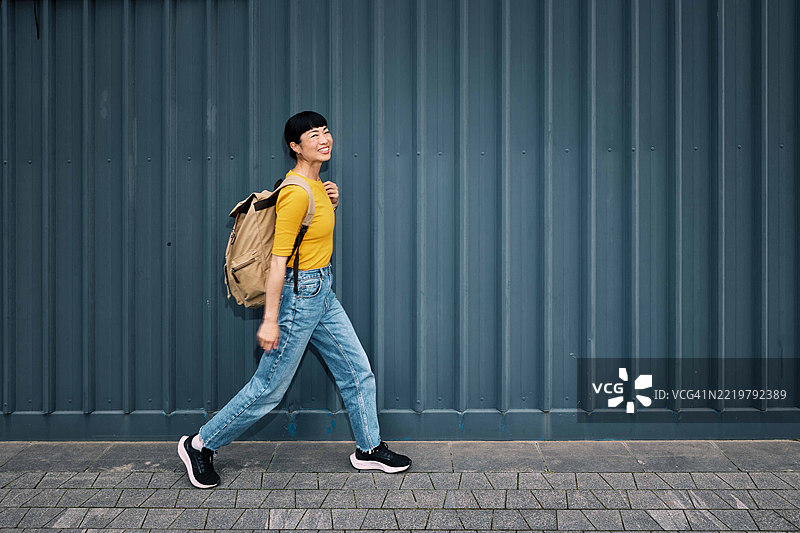 背着背包的日本女性在金属墙旁走。图片素材