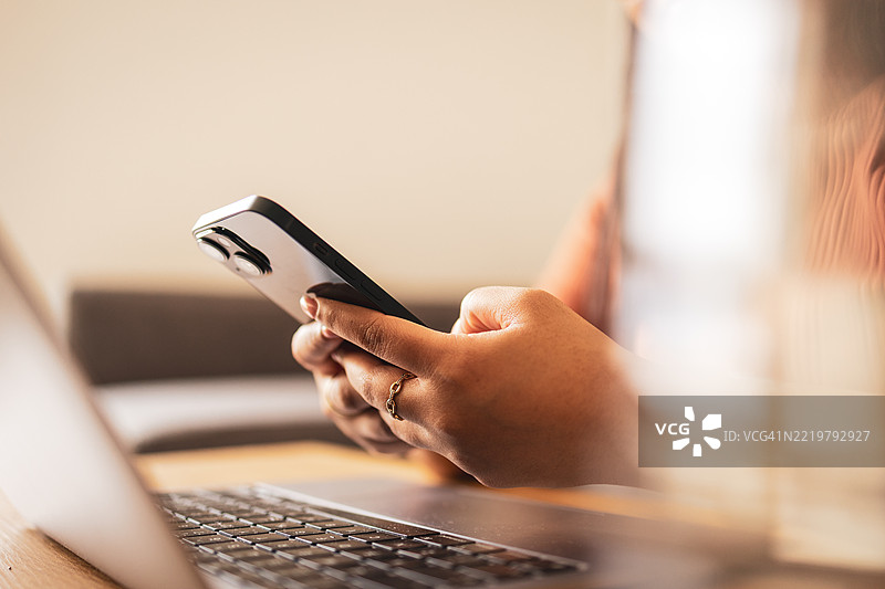 在桌子上使用笔记本电脑时，正在用智能手机的人图片素材