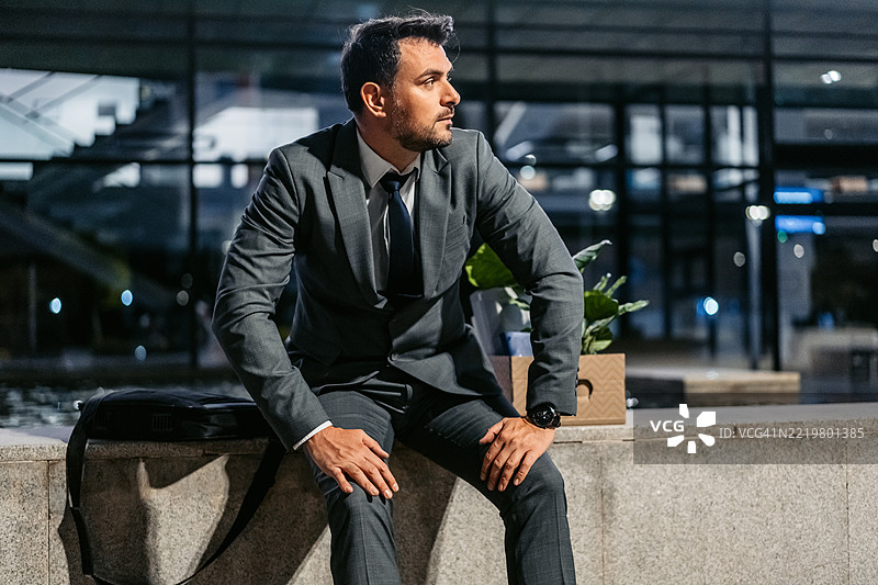 悲伤的中年商人坐在公司大楼前，手里拿着一箱办公用品。图片素材