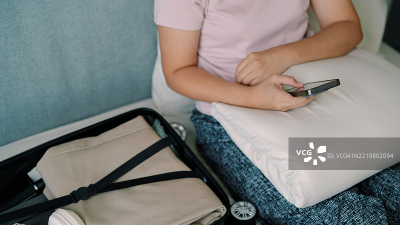 亚洲女性正在使用手机并准备行李旅行图片素材