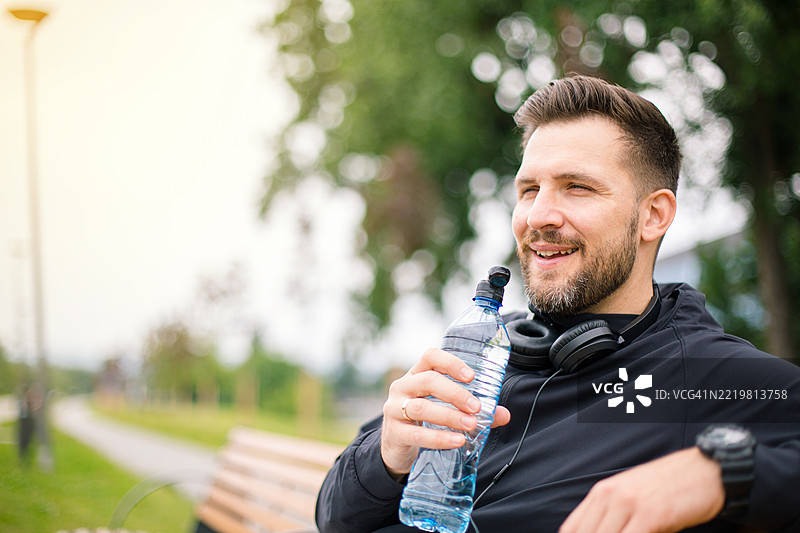 年轻运动员在公园的长椅上喝水休息图片素材