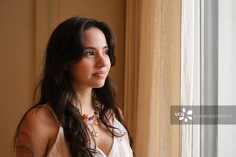 年轻的拉丁裔女性望着窗外，思考未来图片素材