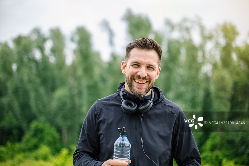 快乐的男性跑者在户外训练后手持水瓶图片素材