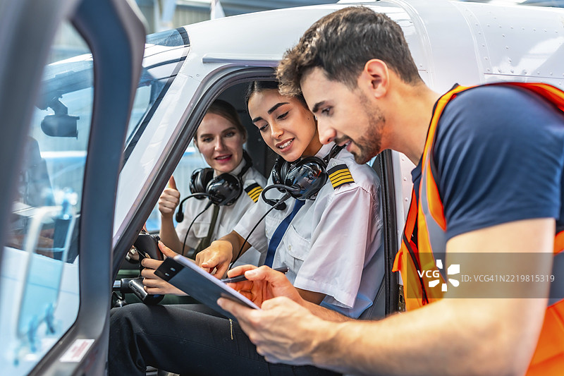 飞机维修工程师向两位微笑的女飞行员简报，她们坐在驾驶舱内竖起大拇指。图片素材