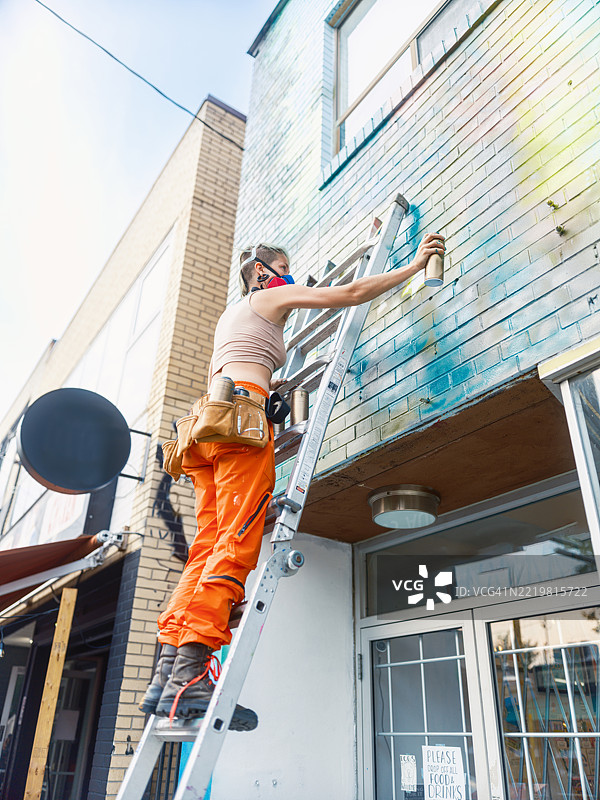 年轻女性在城市建筑的外立面上创作壁画图片素材