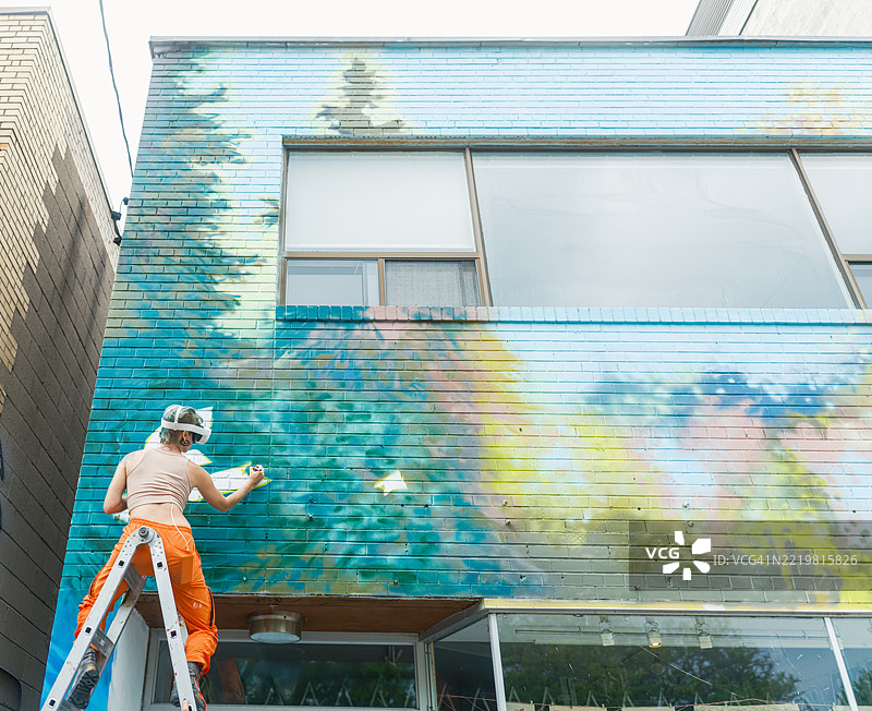 戴着虚拟现实眼镜的年轻女性在城市建筑的外立面上创作壁画图片素材