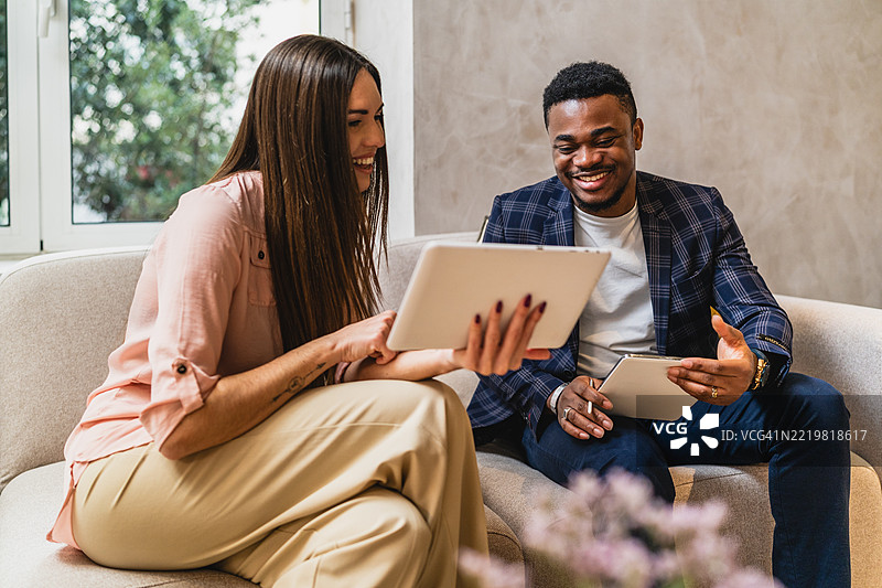 微笑的商务同事们在现代办公室的沙发上使用数字平板电脑图片素材