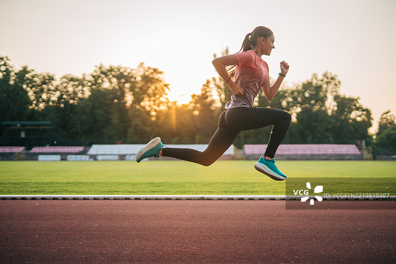 年轻女性运动员在日落时分的跑道上奔跑图片素材