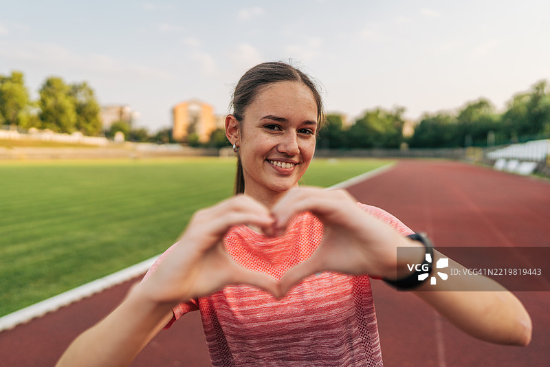 年轻的运动女性在跑道上用双手做出心形手势图片素材