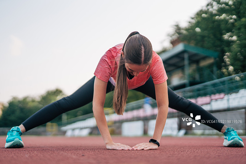 年轻运动员在体育场跑步前拉伸腿部图片素材