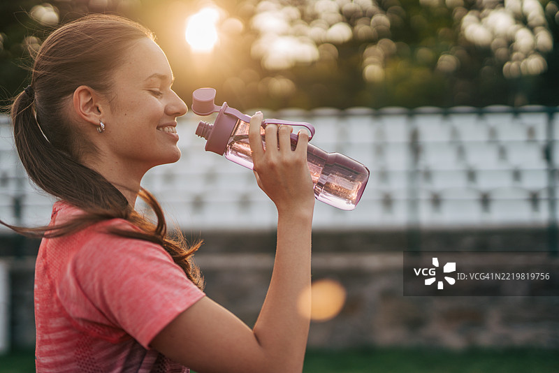 年轻女运动员在日落时分训练后喝水图片素材