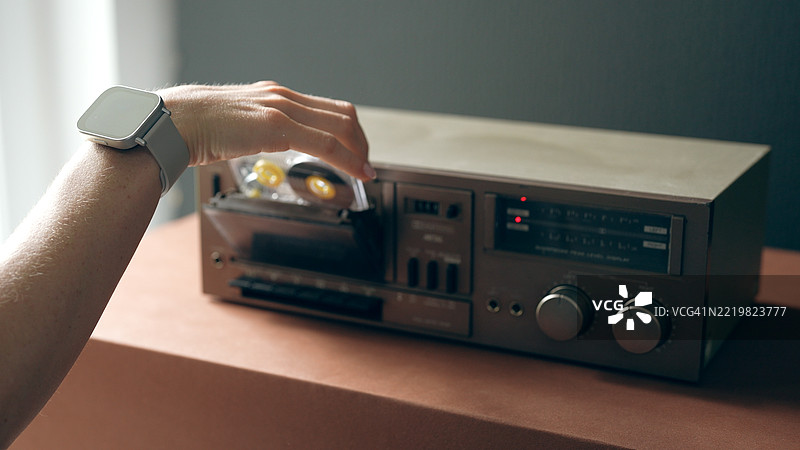 一只戴着智能手表的女性手将磁带插入录音机。图片素材