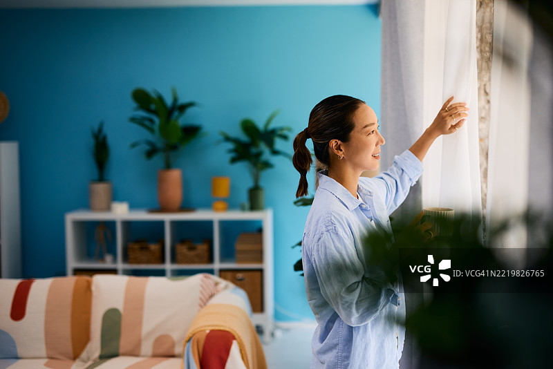 年轻女性在现代公寓中拉开窗帘，向外望去图片素材