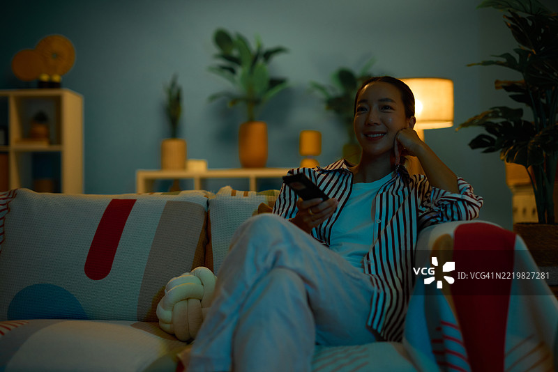 年轻女性在沙发上放松，晚上看电视图片素材