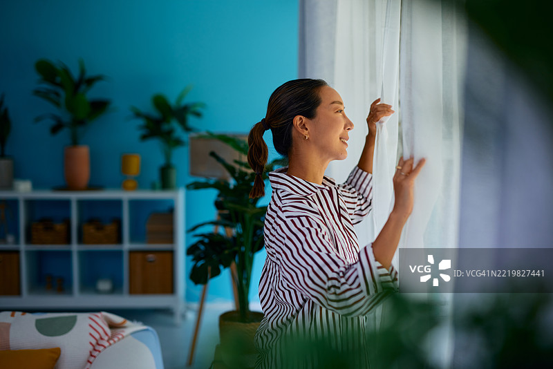 年轻女性在现代公寓中拉开窗帘，向外望去图片素材