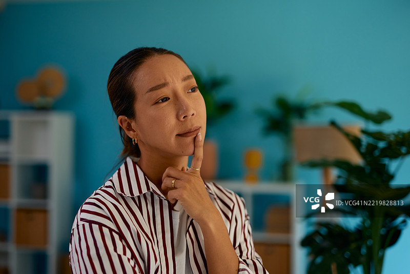 年轻的亚洲女性用手指托着下巴，思考在家中的决策。图片素材