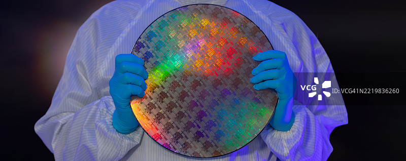 电子制造厂的半导体生产。工人或工程师穿着医疗防护服或白色工作服，手持硅晶圆。图片素材