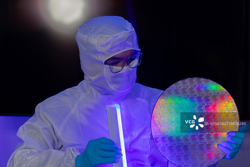 电子制造厂的半导体生产。工人或工程师穿着医疗防护服或白色工作服，手持硅晶圆。图片素材