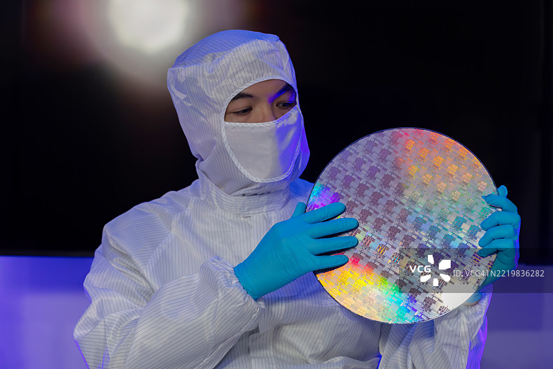 电子制造厂的半导体生产。工人或工程师穿着医疗防护服或白色工作服，手持硅晶圆。图片素材