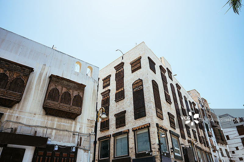 在吉达的历史区阿尔巴拉德，清澈的蓝天下，街景中有沙特阿拉伯国旗、棕榈树和传统建筑。图片素材