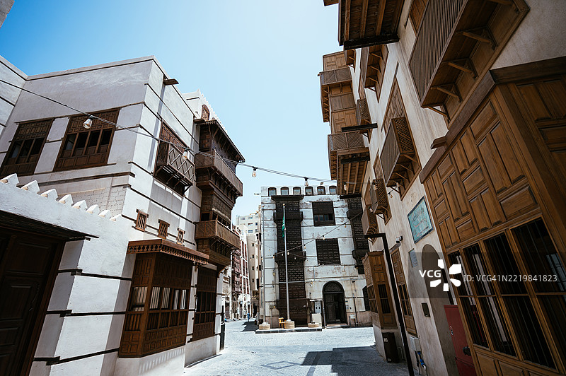 在吉达的历史区阿尔巴拉德，清澈的蓝天下，街景中有沙特阿拉伯国旗、棕榈树和传统建筑。图片素材