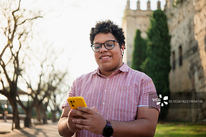 年轻男子在城市公园里使用智能手机并佩戴耳机图片素材